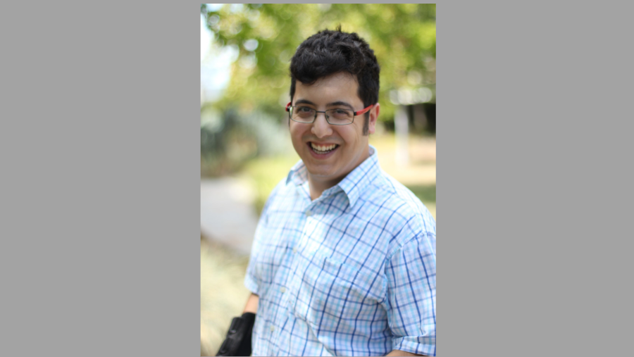 Main in plaid shirt standing with green tree in background